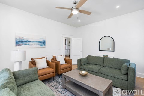 A living room with a green couch, a brown chair, and a painting of a mountain scene on the wall.