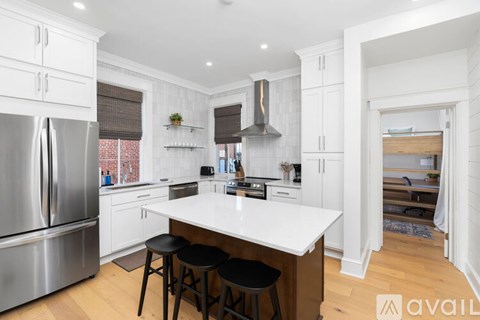 A kitchen with white cabinets and a large island with black stools.
