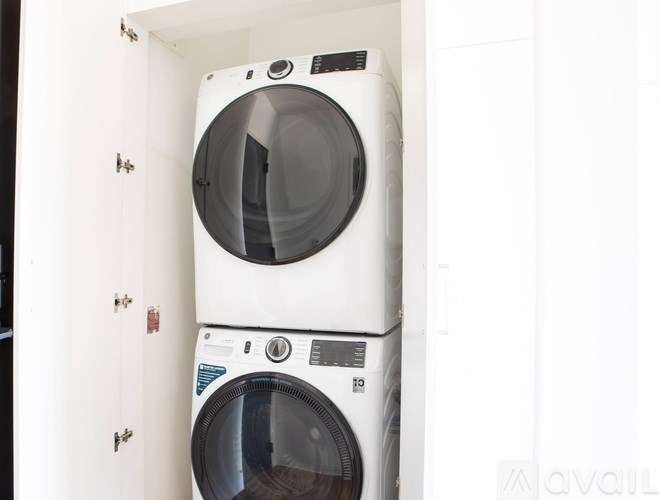 Two white washing machines stacked on top of each other in a cabinet.