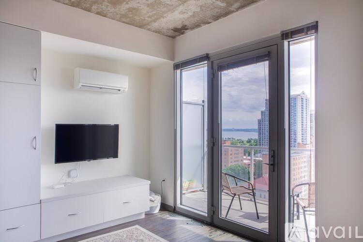 A modern living room with a television, a white cabinet, and a sliding glass door leading to a balcony.