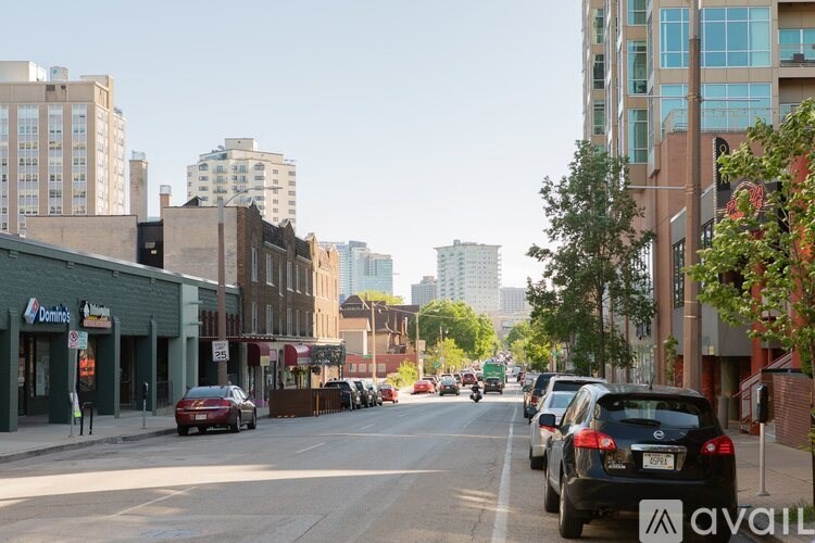 A city street with cars parked on the side and buildings in the background.