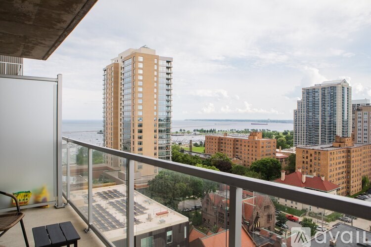 A balcony with a table and chairs overlooks a cityscape with buildings and a body of water.