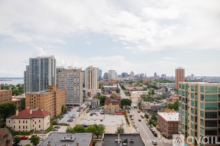 A cityscape with a mix of modern and older buildings, a parking lot, and a cloudy sky.