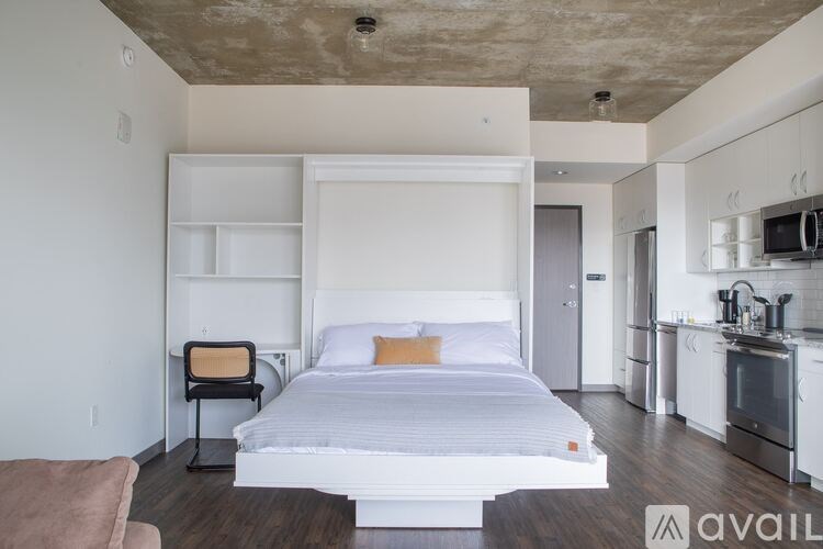 A bedroom with a bed, chair, and a kitchen area.