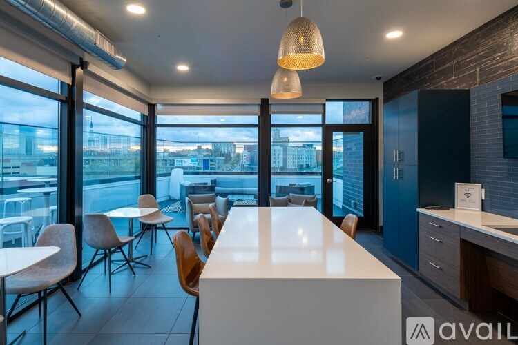 A modern office space with a long white table and chairs, a hanging light fixture, and a view of the city through large windows.