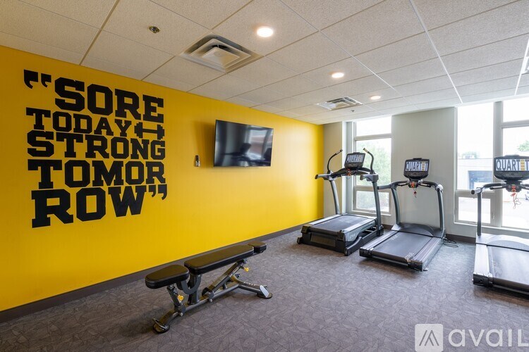 A gym room with a yellow wall that says "sore today, strong tomorrow" and a row of treadmills.