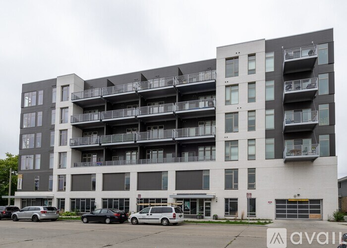 A large apartment building with multiple balconies and cars parked in front.