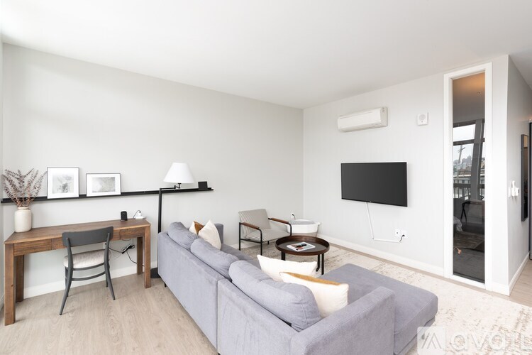 A living room with a grey couch, a wooden table, and a flat screen TV mounted on the wall.