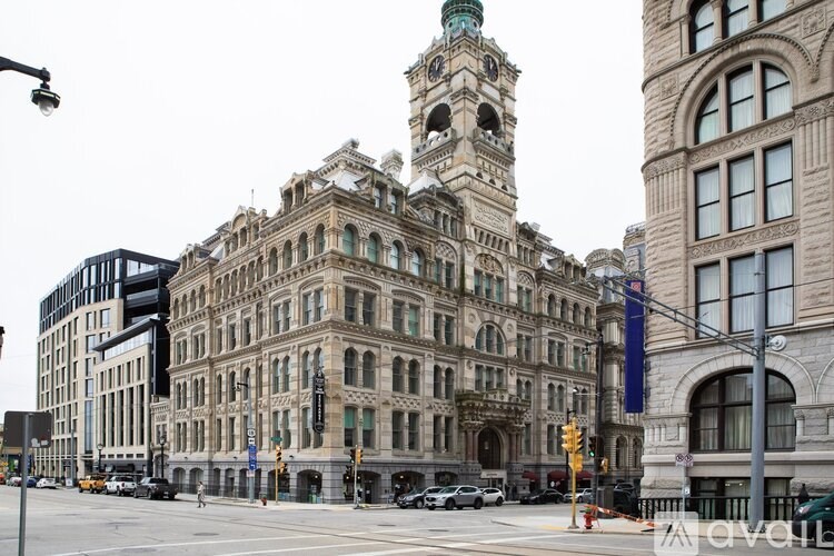 A large, ornate building with a clock tower stands in the middle of a city intersection.