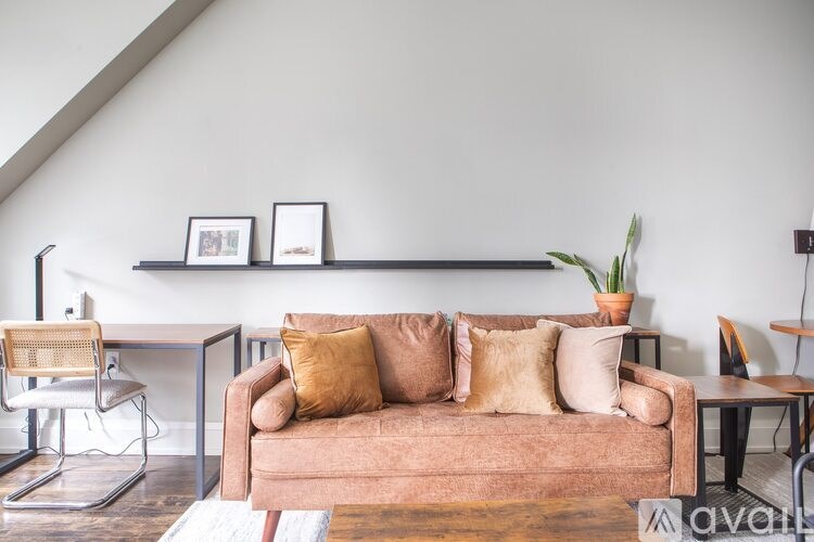 A living room with a brown couch, a chair, a desk, and a shelf with picture frames.