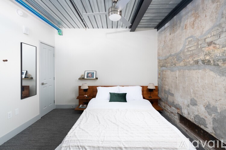 A bedroom with a white bed and a stone wall.