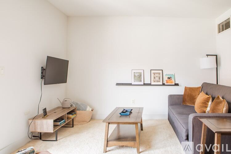 A living room with a grey couch, a wooden coffee table, and a flat screen TV mounted on the wall.
