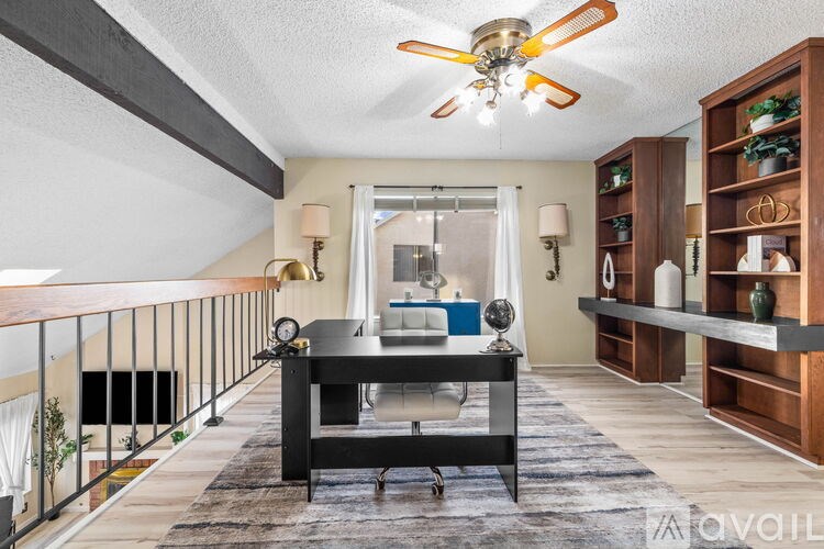 A room with a desk, a chair, a ceiling fan, and a bookshelf.
