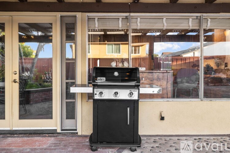 A black outdoor grill is in front of a glass door.