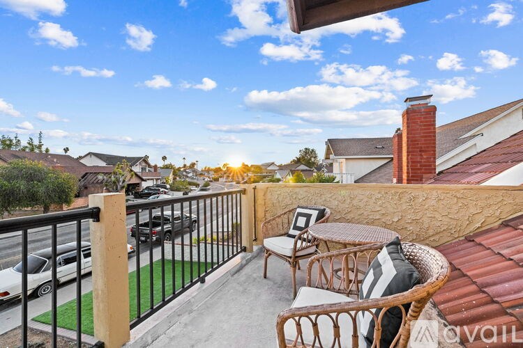 A balcony with a table and chairs overlooks a street with cars and houses.