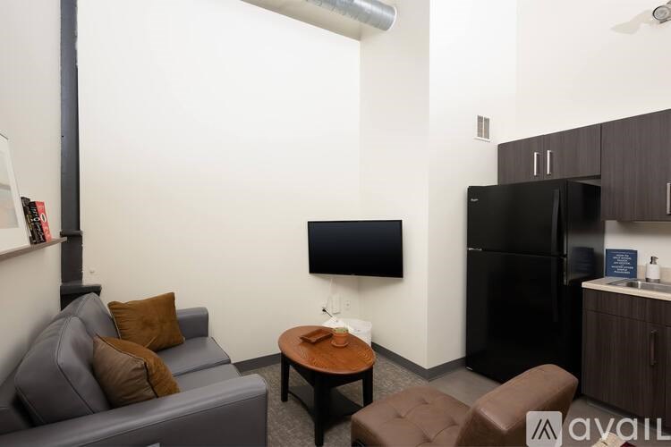 A living room with a grey couch, a black refrigerator, a black TV and a brown leather chair.