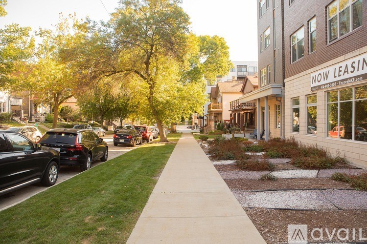 A street with cars parked on the side and a building that says "NOW LEASING" in front.