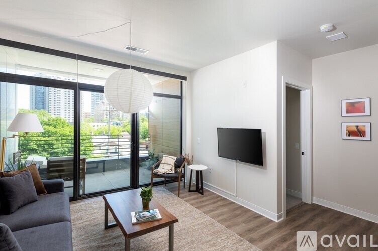 A living room with a grey couch, a wooden coffee table, a flat screen TV, and a large window with a view of the city.