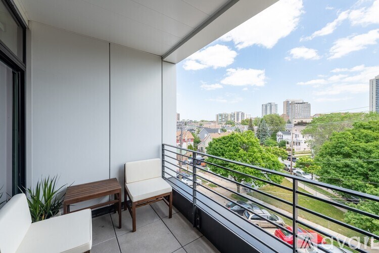 A balcony with a table and chairs overlooking a parking lot and buildings.