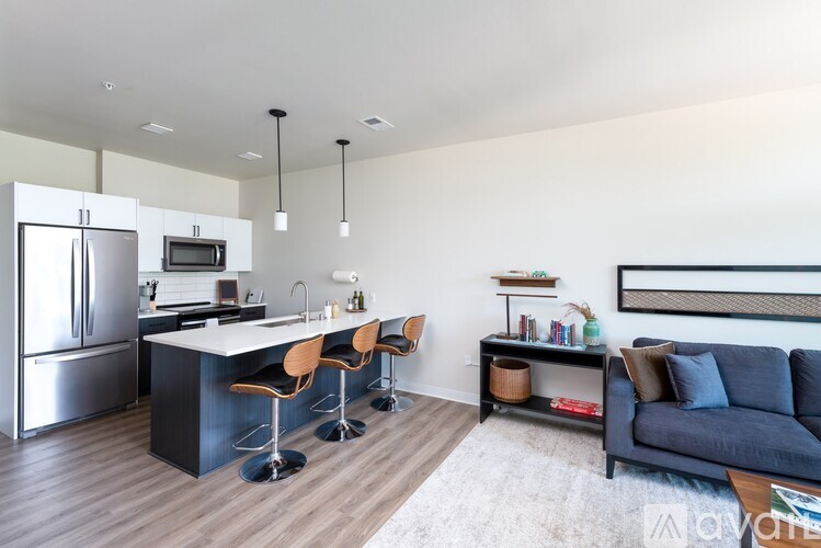 A modern kitchen with a refrigerator, bar stools, and a couch.