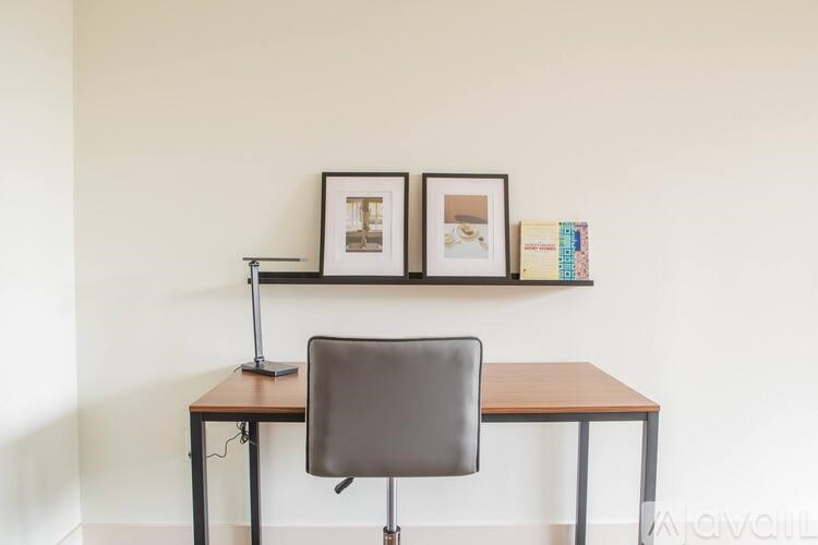 A brown desk with a black chair and a lamp on it.