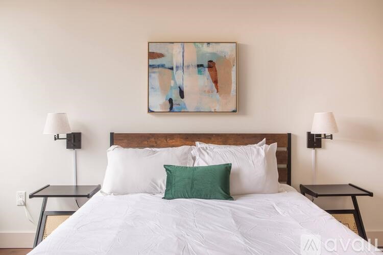 A bed with a white comforter and a green pillow is flanked by two black lamps.