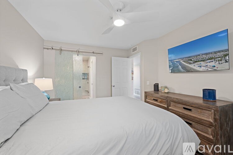 A bedroom with a large bed, a ceiling fan, and a painting of a beach scene on the wall.