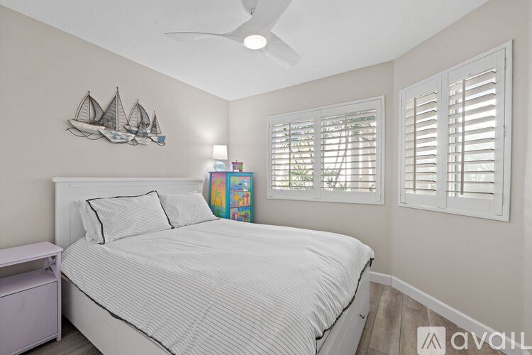 A bedroom with a bed, a ceiling fan, and a wall decoration.