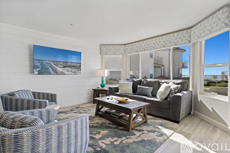 A living room with a grey couch, a wicker chair, and a large picture of a beach on the wall.