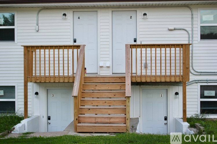 A white house with a wooden deck and stairs leading to the front door.