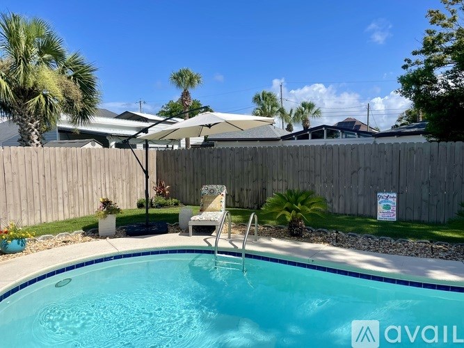 A pool with a chair and umbrella in the foreground and a fence in the background.