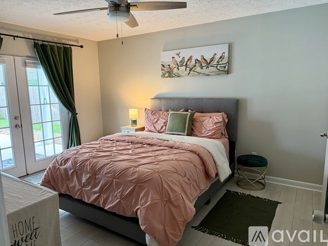 A bedroom with a bed covered in a pink comforter and a ceiling fan above it.