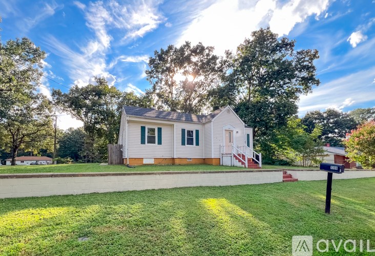 A house with a white exterior and green shutters is surrounded by a grassy lawn and trees.