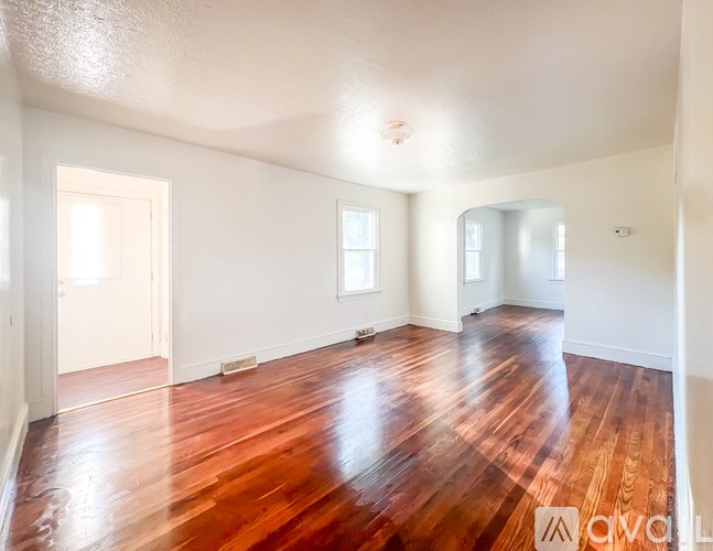 A room with carpeted floor and two windows with red curtains.