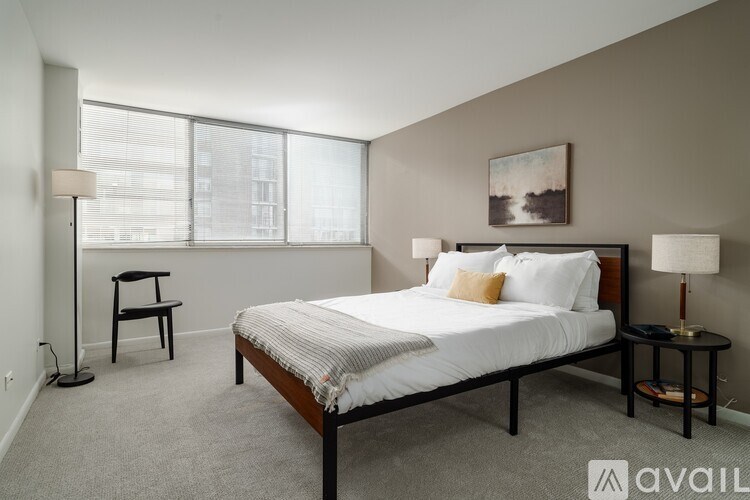 A bedroom with a large bed, a chair, and a window with blinds.