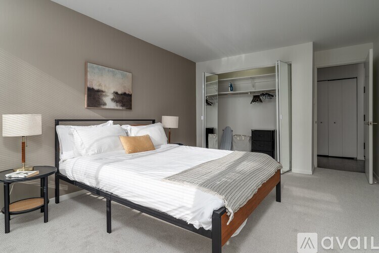 A bedroom with a large bed, a nightstand with a lamp, and a painting on the wall.