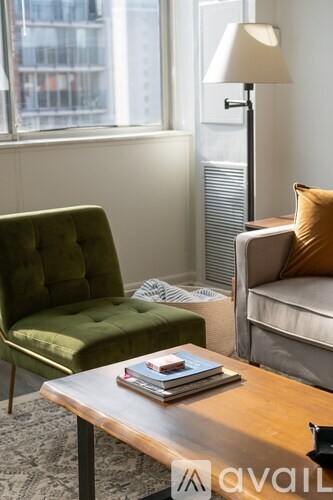 A green chair sits next to a white sofa with a lamp and a window in the background.