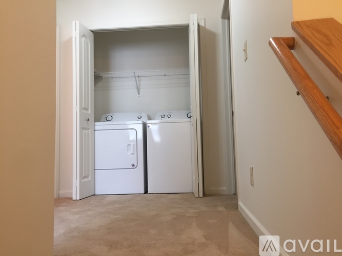A kitchen with a white fridge and a white dishwasher is in a room with a staircase.