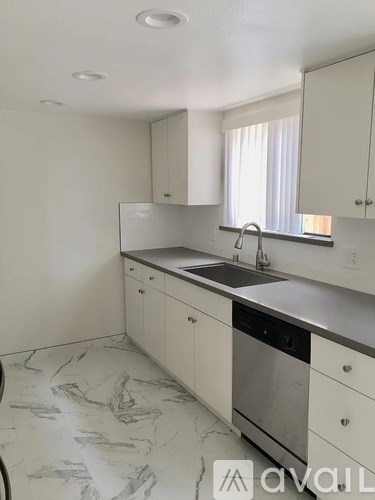 A kitchen with white cabinets and marble flooring.