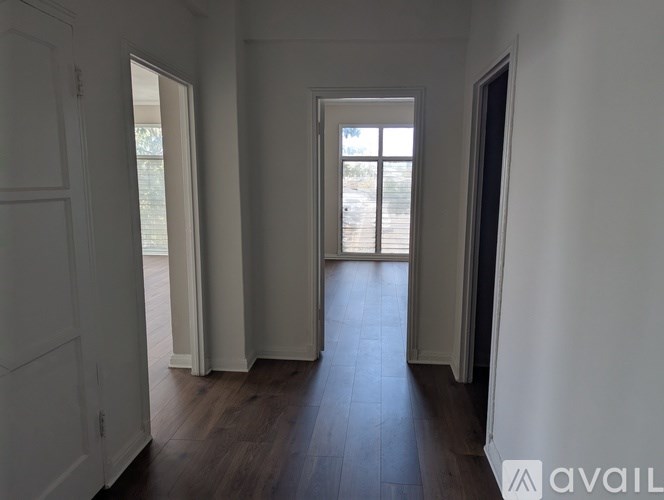 A room with white walls and wooden flooring, with a door on the right and a window on the left.