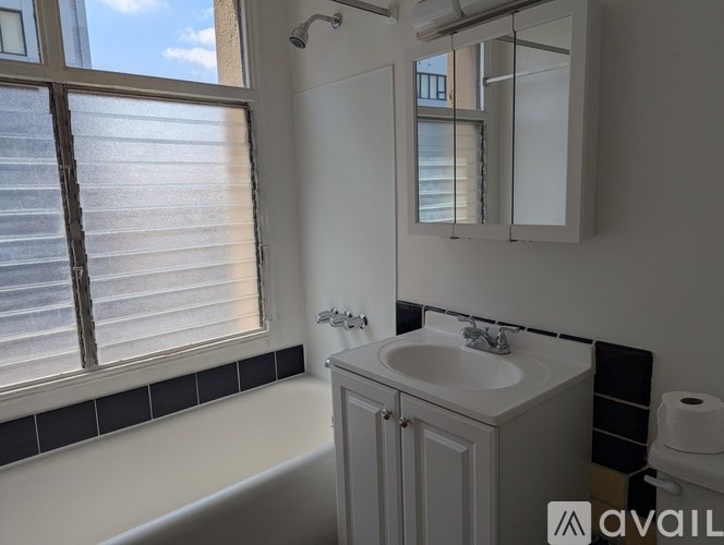 A bathroom with a white tub, sink, and a window with blinds.