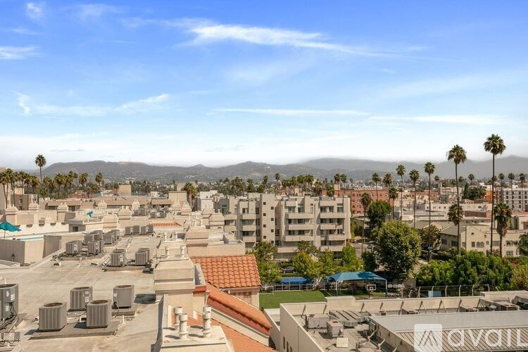 A view of a cityscape with buildings, trees, and mountains in the distance.