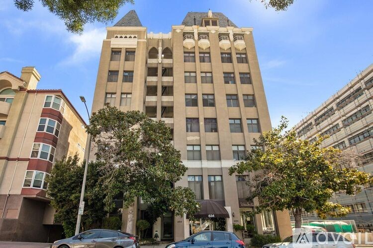 A tall beige building with a pointed roof and a tree in front of it.