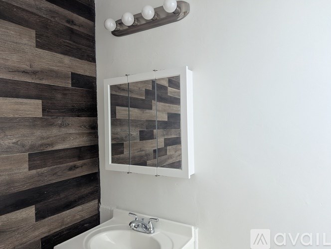 A bathroom with a white sink and a mirror with a wooden panel on the wall.
