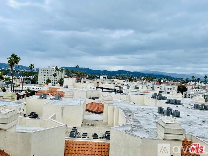 A cityscape with buildings and palm trees under a cloudy sky.