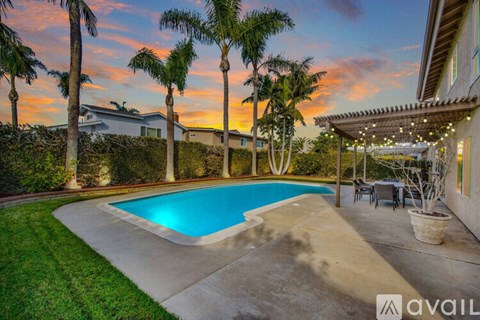 A pool surrounded by palm trees and a house with a patio.