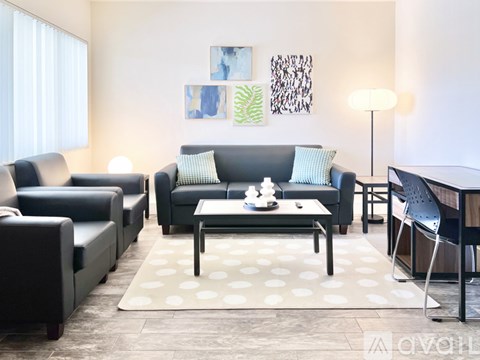 A living room with a black couch, a grey armchair, a black chair, a coffee table, and a rug with white polka dots.