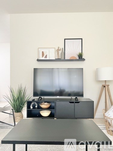 A black television sits on a black cabinet with a black table in front of it.