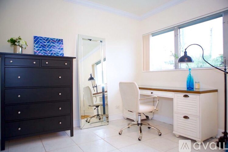 A black dresser sits next to a white chair and desk in a room.