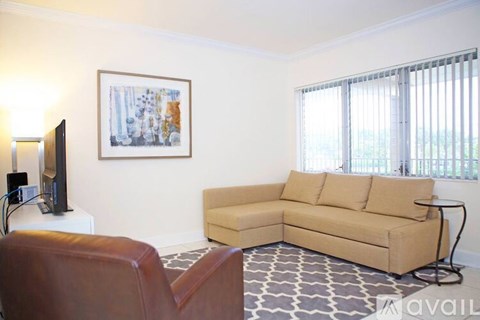 A living room with a tan couch, a brown leather chair, and a painting on the wall.